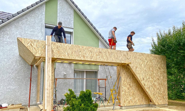 Des ouvriers construisent une rampe et une plateforme en bois sur le côté d’une maison blanche