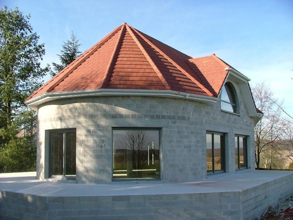 Maison ronde en pierre avec un toit de tuiles rouges et de grandes fenêtres, vue de l’extérieur