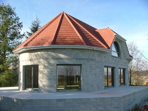 Maison ronde en pierre avec un toit de tuiles rouges et de grandes fenêtres, vue de l’extérieur