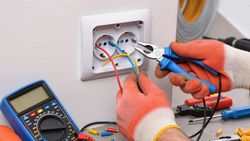 Un électricien effectue le câblage d'une prise murale avec des outils et un multimètre à portée de main.
