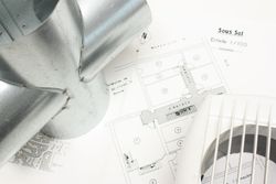 Des éléments de conduits métalliques, un plan d'étage et un ventilateur sur une surface, suggérant la conception d'un système de ventilation.