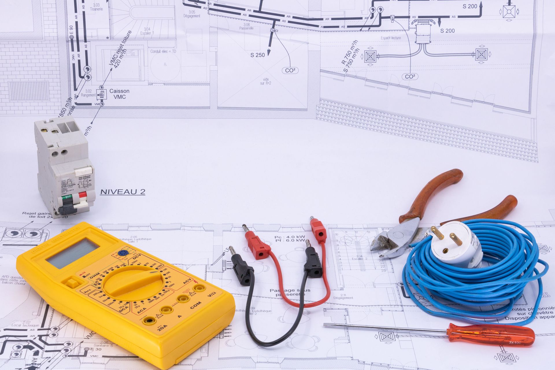 Outils de test électrique figurant sur un plan, notamment un multimètre, une pince ampèremétrique, des sondes et un câble enroulé.