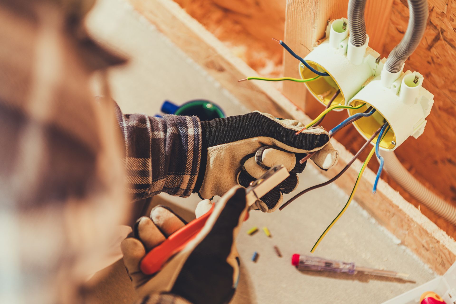 Des mains câblent une prise électrique avec des outils sur une surface en bois.
