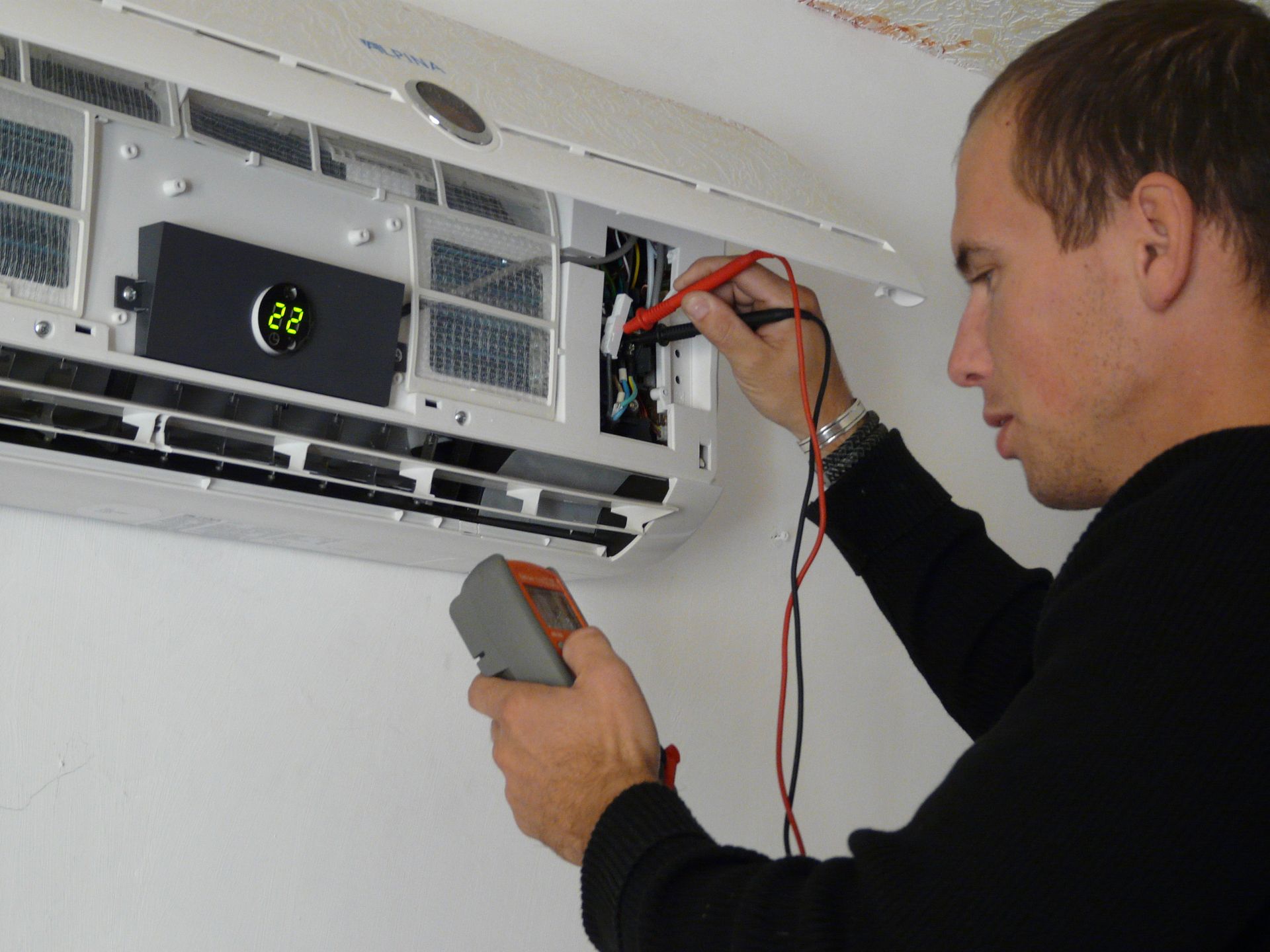 Un technicien teste un climatiseur mural ouvert à l'aide d'un multimètre.