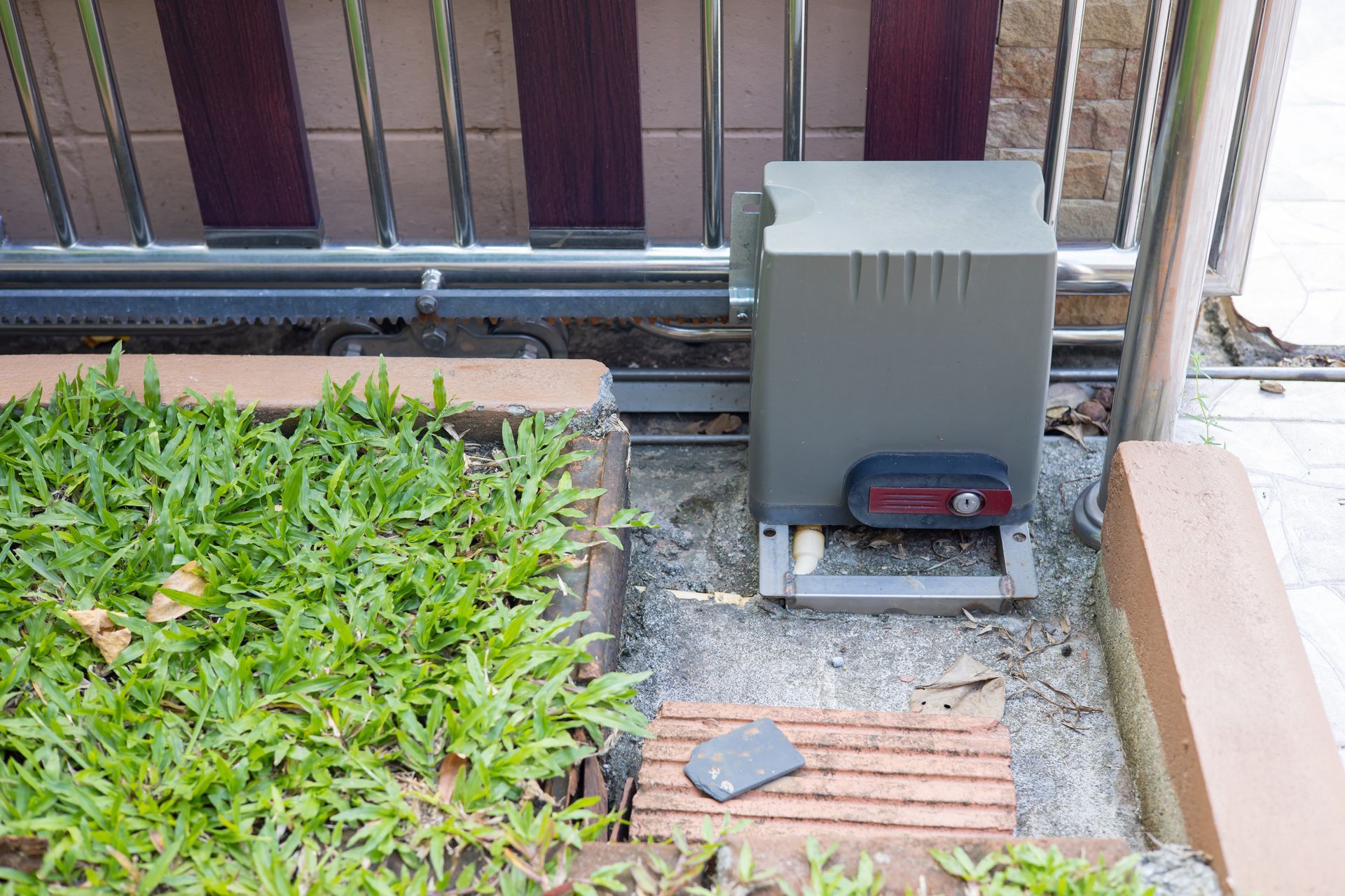 Un boîtier électrique à côté d'une clôture, avec des briques et un petit objet au sol.