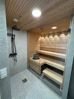 Moderni sauna, jossa on puulauteet, laattalattia ja lämmin valaistus suihkutilassa