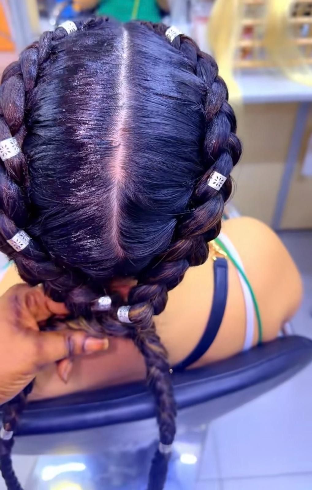 Vista aérea de una persona sentada en una silla de peluquería con una trenza oscura con detalles plateados.
