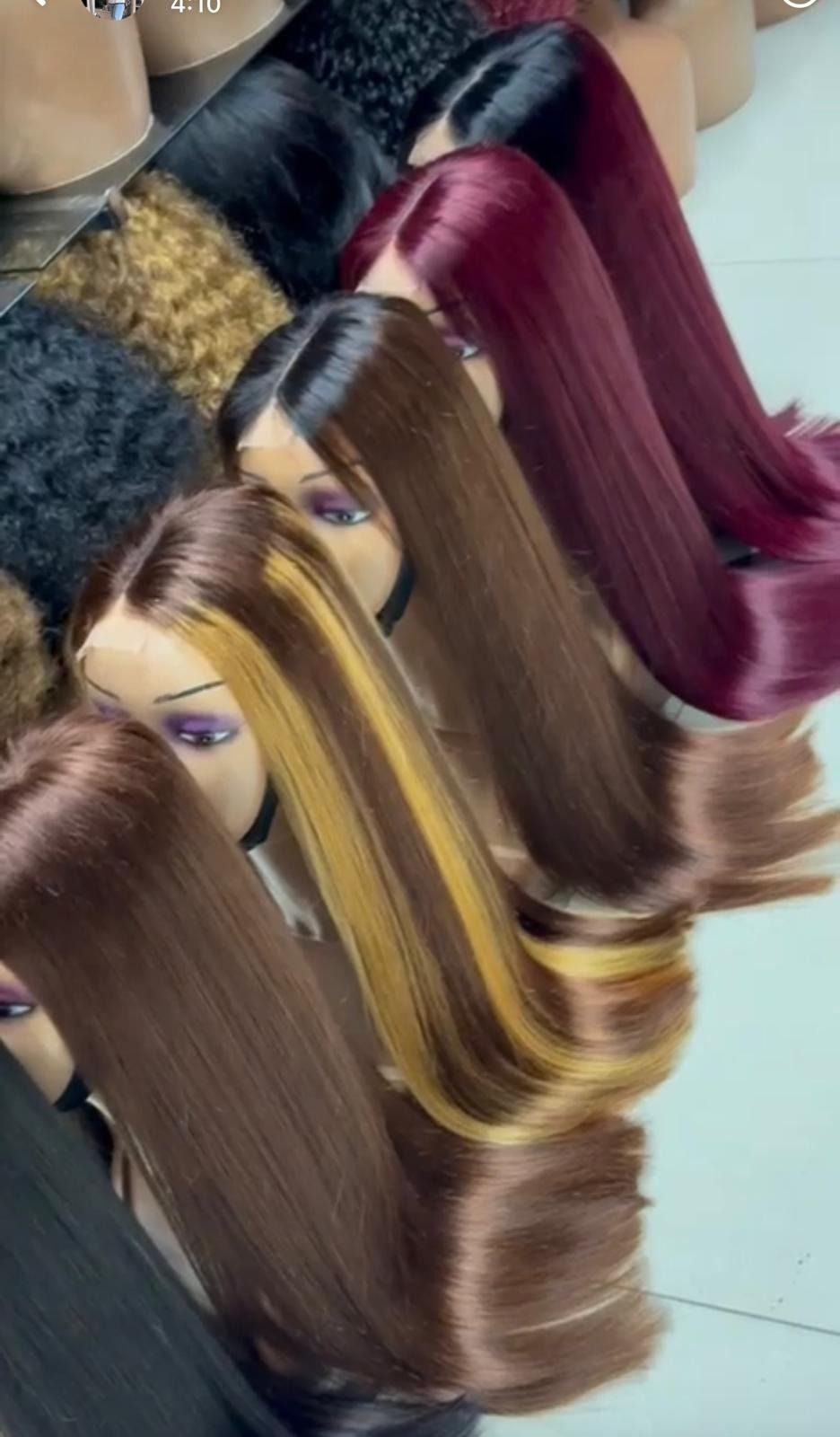 Hileras de pelucas de cabello largo y ondulado en tonos rubios, castaños, negros y burdeos sobre cabezas de maniquí.