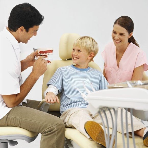 Un niño pequeño está sentado en una silla dental hablando con un dentista.