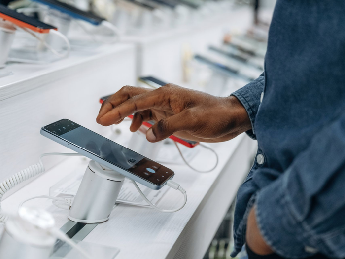 Une main touche un smartphone sur un présentoir dans un magasin d'électronique.