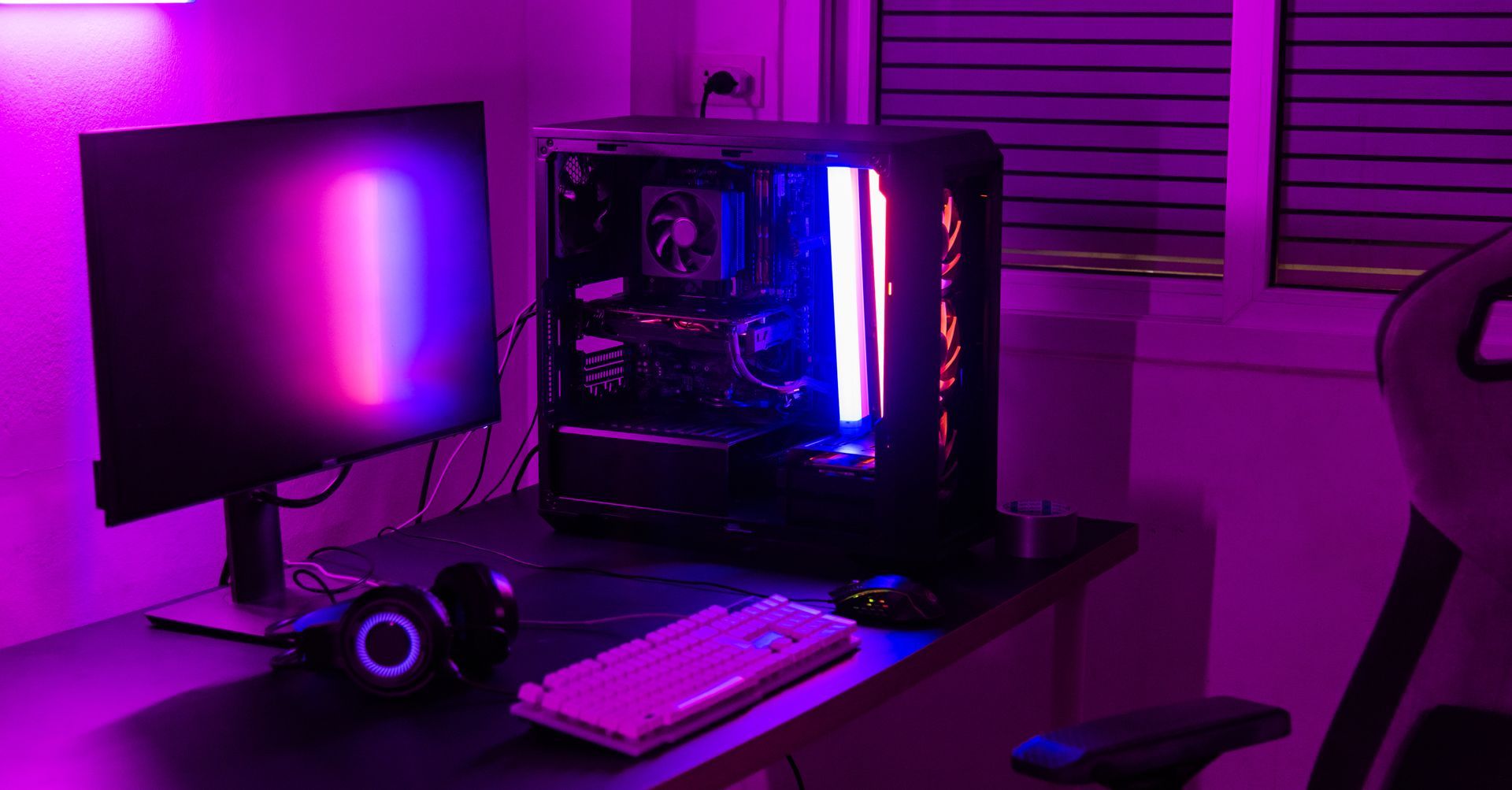 Bureau gaming rétroéclairé en violet avec écran, tour PC, clavier et casque audio.