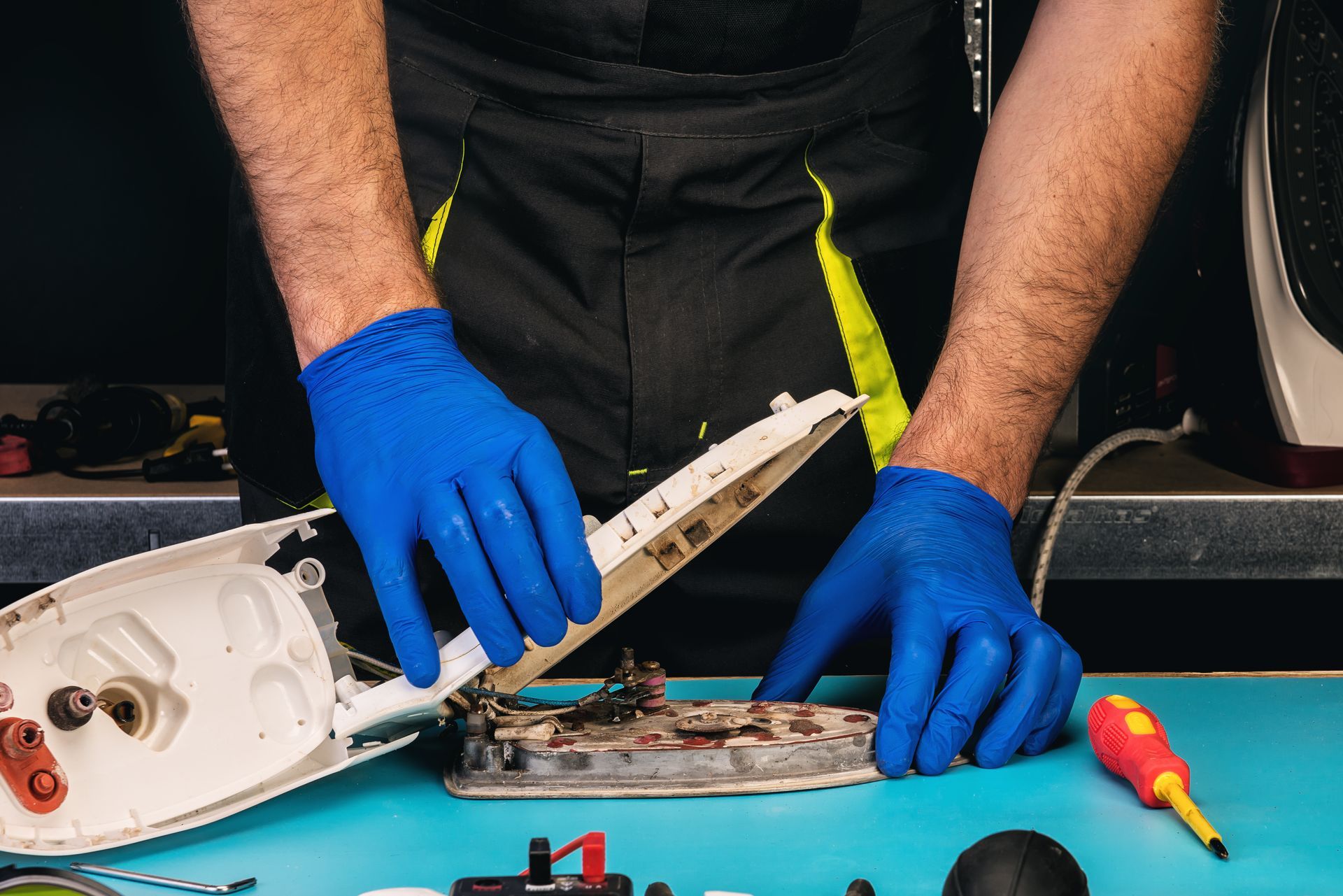 Un technicien portant des gants bleus répare un fer à repasser.