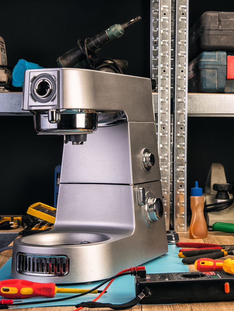Machine à expresso argentée sur un établi avec des outils et des câbles dans un atelier.