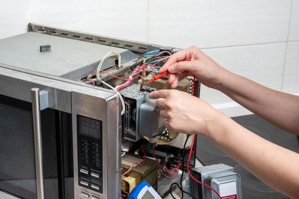 Des mains réparent le câblage à l'intérieur d'un four à micro-ondes sur un comptoir.