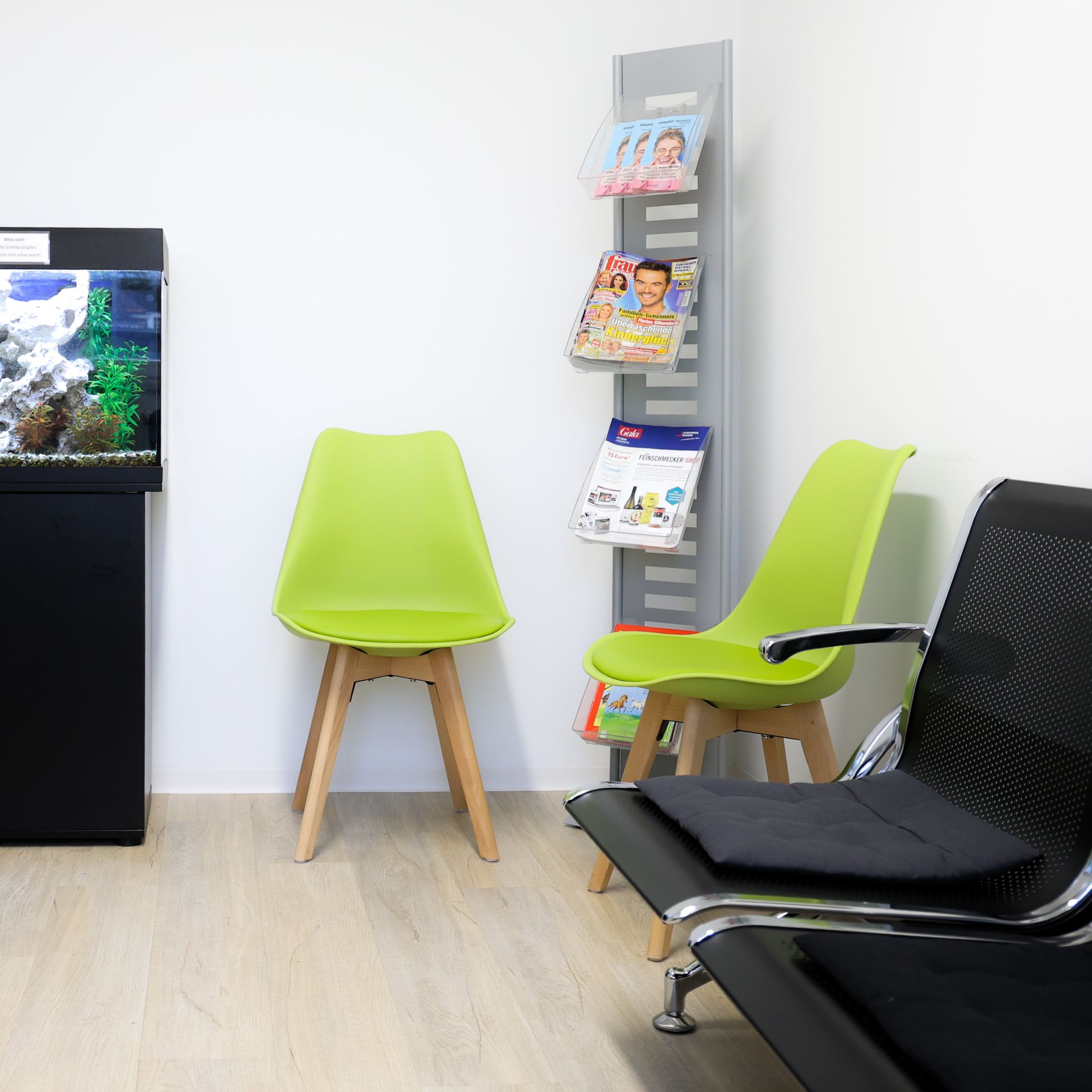 Wartezimmer mit grünen Stühlen, Zeitschriftenständer und Aquarium.
