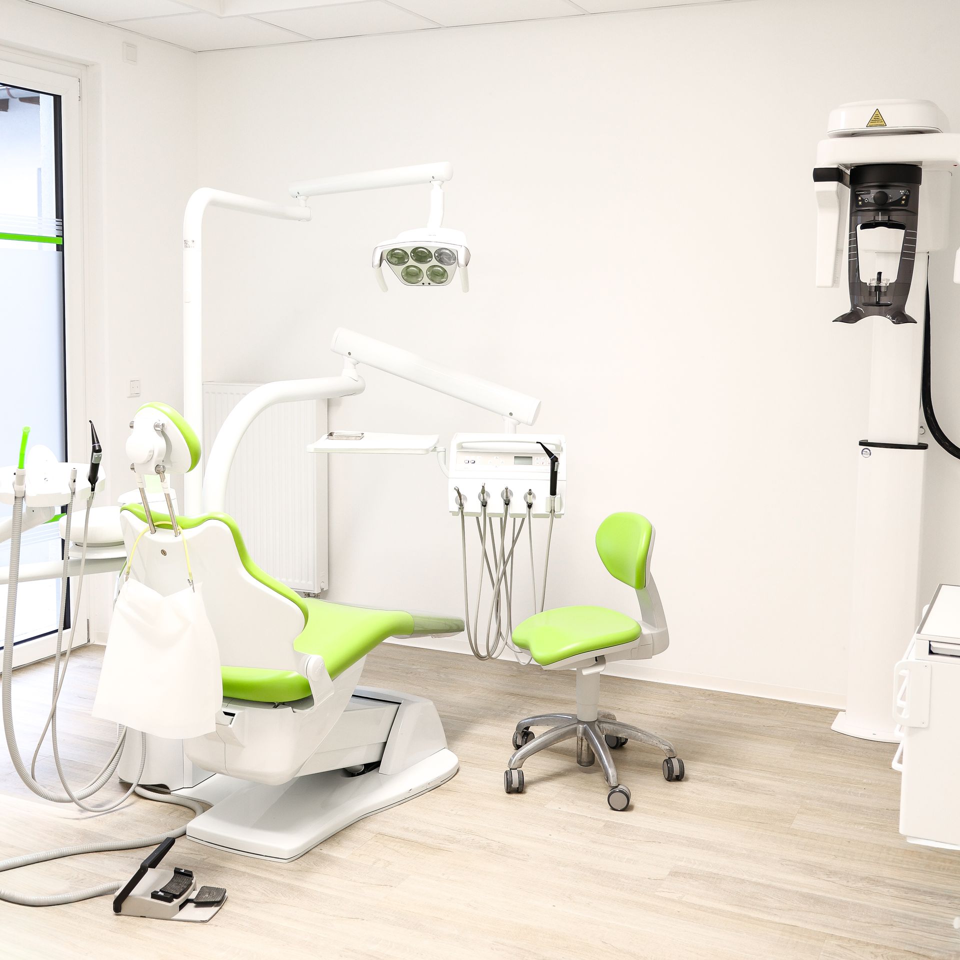 Zahnarztzimmer mit hellgrünem Stuhl, zahnärztlicher Ausrüstung und weißen Wänden.
