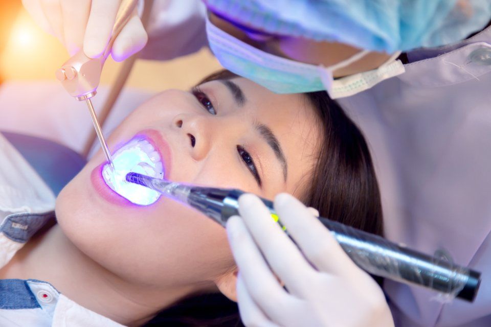 Ein Zahnarzt verwendet in seiner Zahnarztpraxis eine Aushärtungslampe an einem gefüllten Zahn eines Patienten.