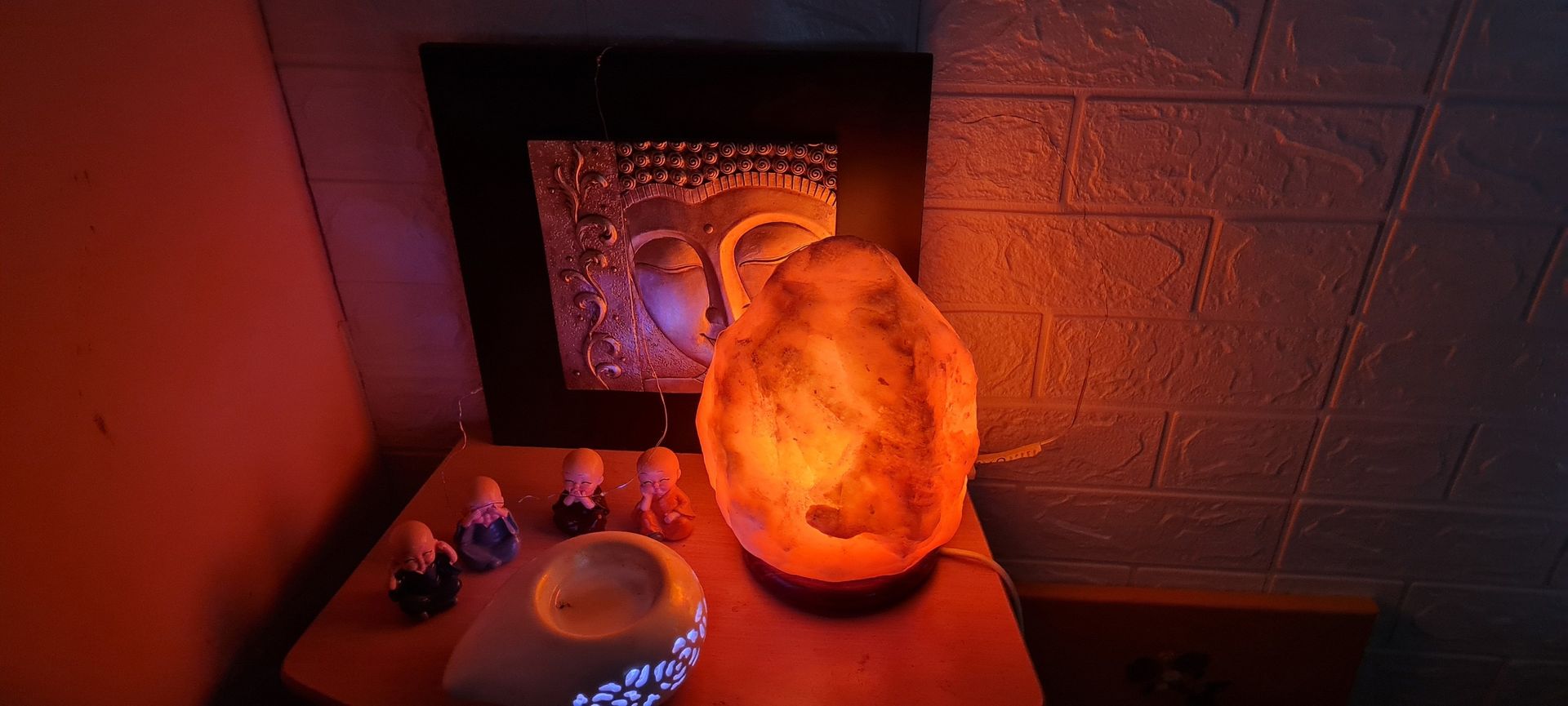 Lampe de sel orange lumineuse sur une table à côté de petites figurines baignées d'une douce lumière rouge.