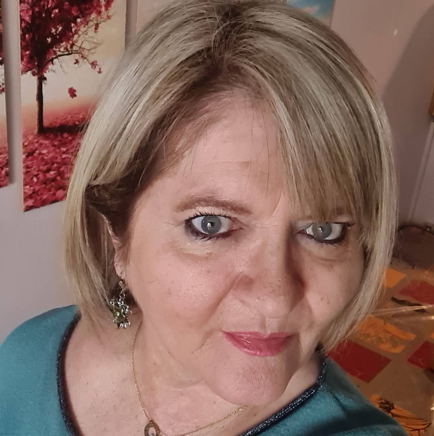 Salle de massage à l'éclairage tamisé, avec un lit, des murs roses et des lampes à la lumière tamisée sur une table d'appoint.