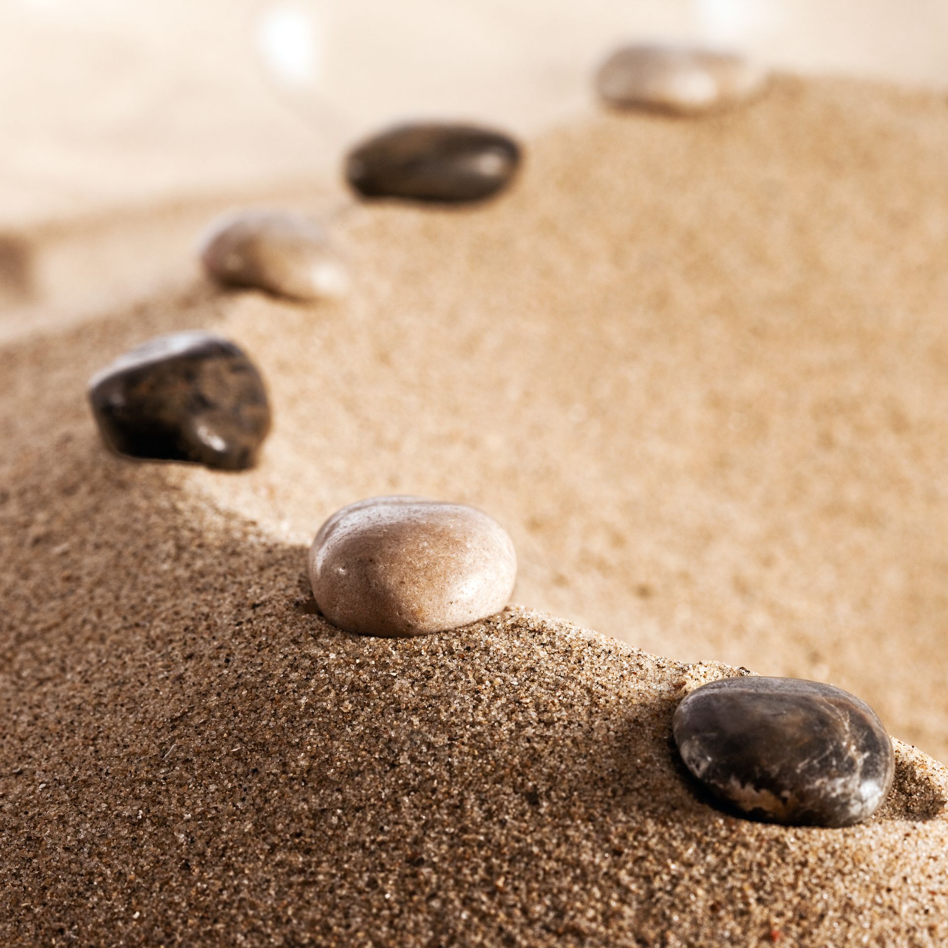 Des galets lisses disposés en ligne sur une plage de sable, formant un chemin sinueux.