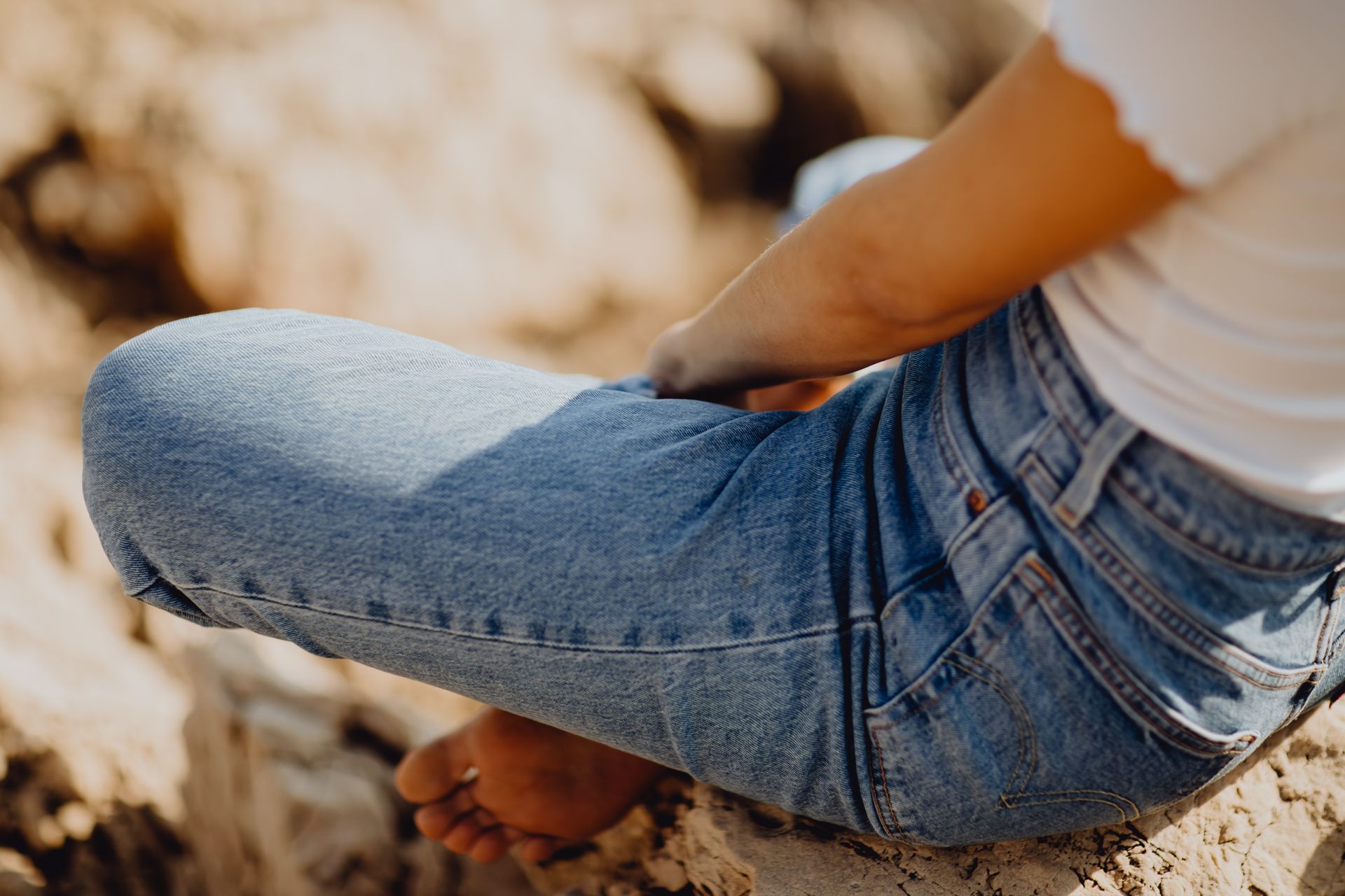 Personne en jean bleu assise sur une surface rocheuse à l'extérieur.