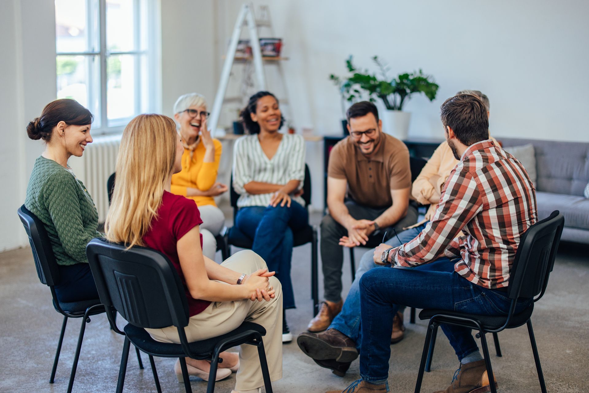Discussion en petit groupe, assis en cercle sur des chaises et un canapé, dans un salon de bureau lumineux.