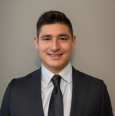 Man in a suit smiles at the camera against a gray background.