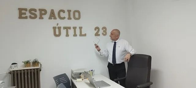Un hombre con traje y corbata está parado frente a una pared que dice espacio util 23