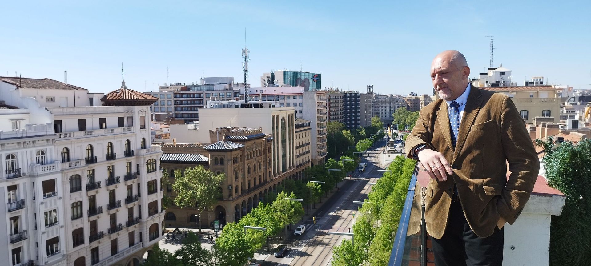 Un hombre con traje y corbata está de pie en un balcón con vistas a una ciudad.