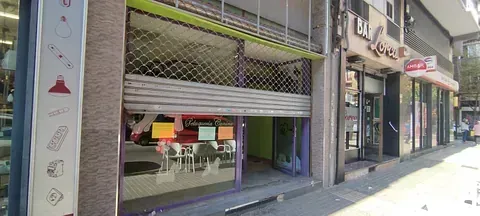 Un frente de tienda con una persiana en la puerta y un cartel en el costado del edificio.