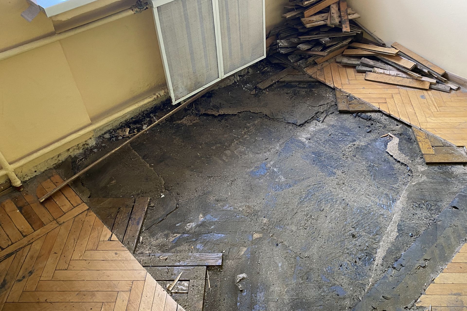 Sol de pièce endommagé avec le revêtement arraché et le sous-plancher à nu près d’un radiateur et d’un mur.