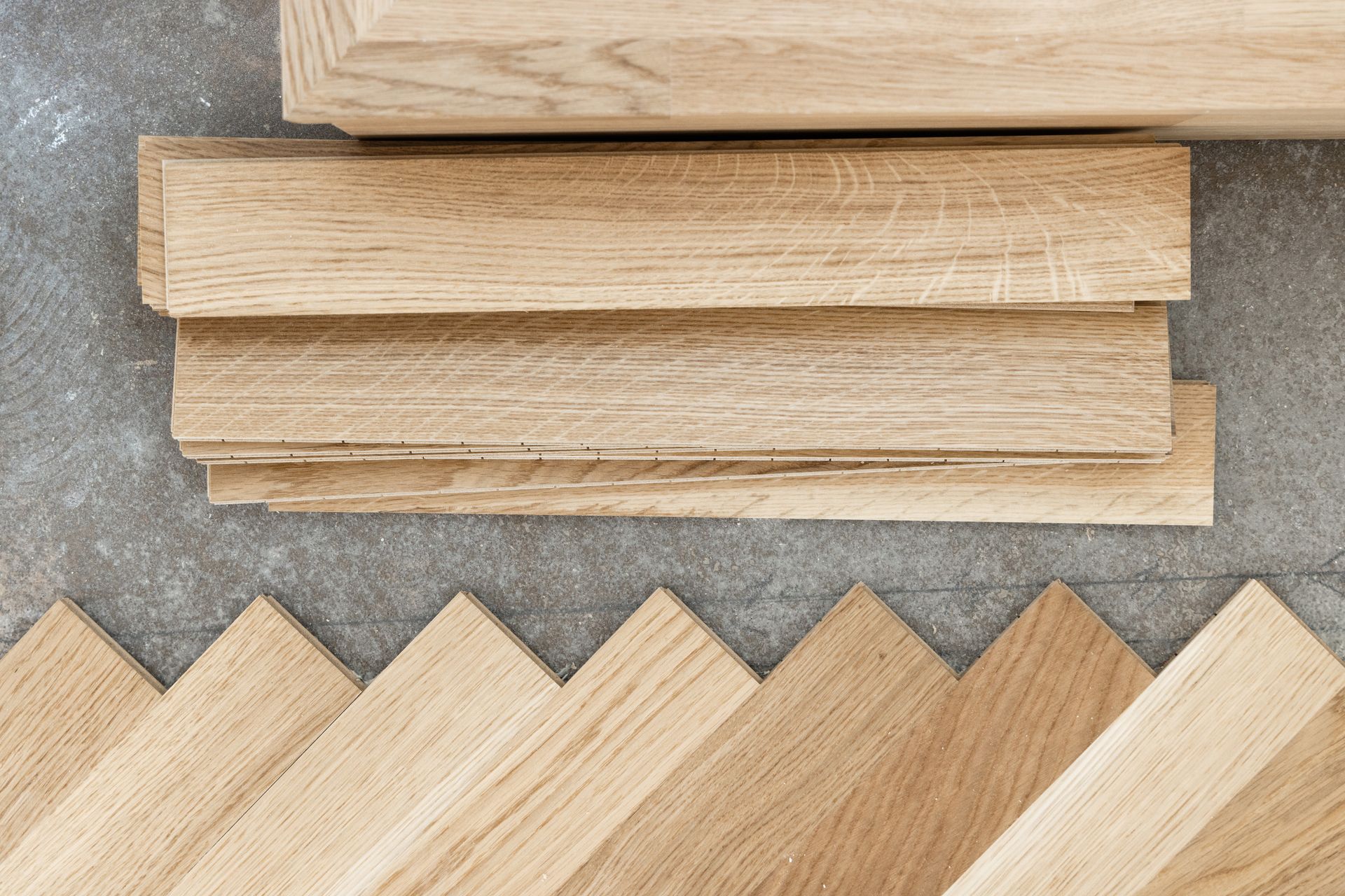 Des lames de bois pour parquet disposés en zigzag sous trois blocs horizontaux, sur un fond gris.