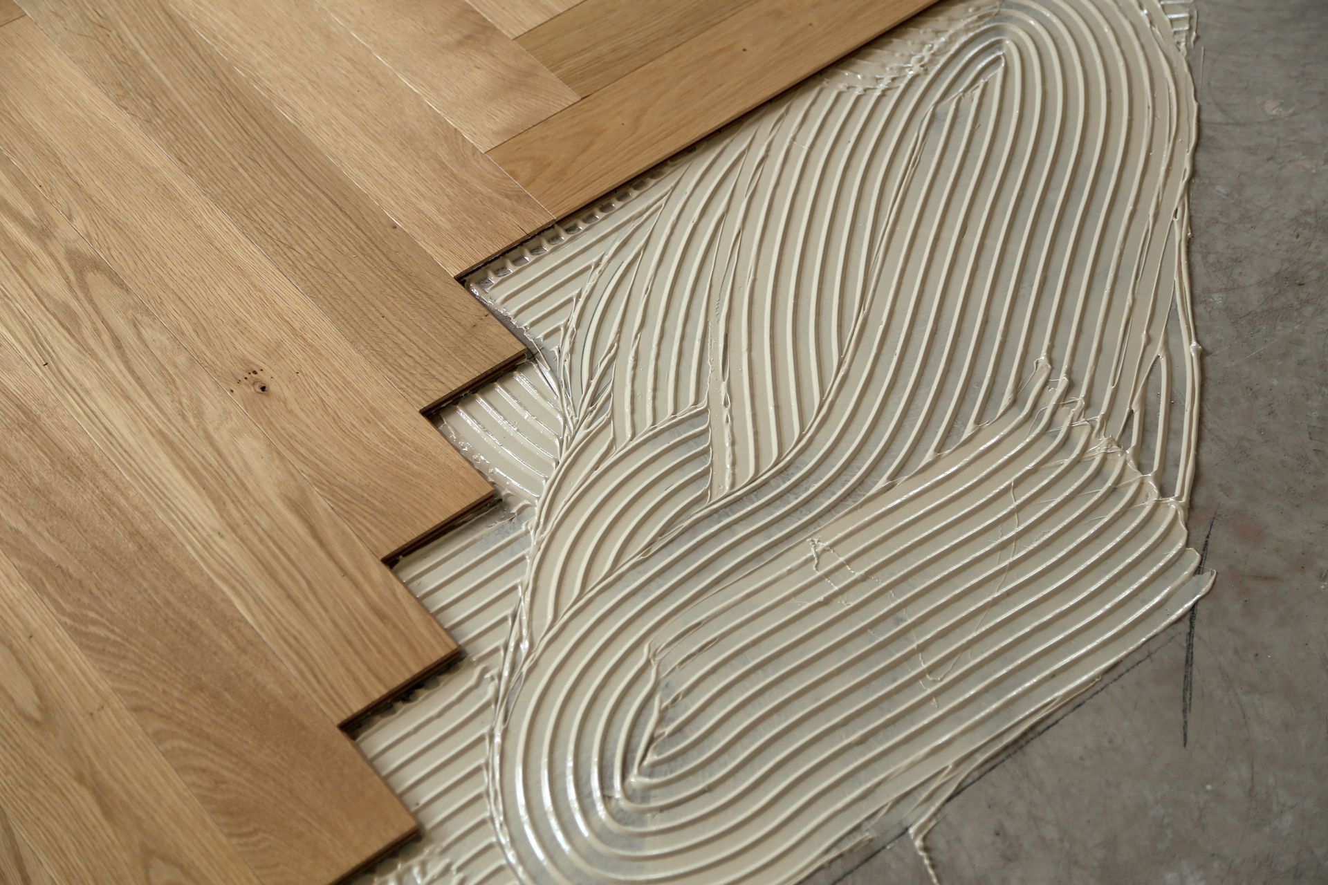 Lames de parquet en bois posées sur de la colle grise étalée sur le sous-plancher.