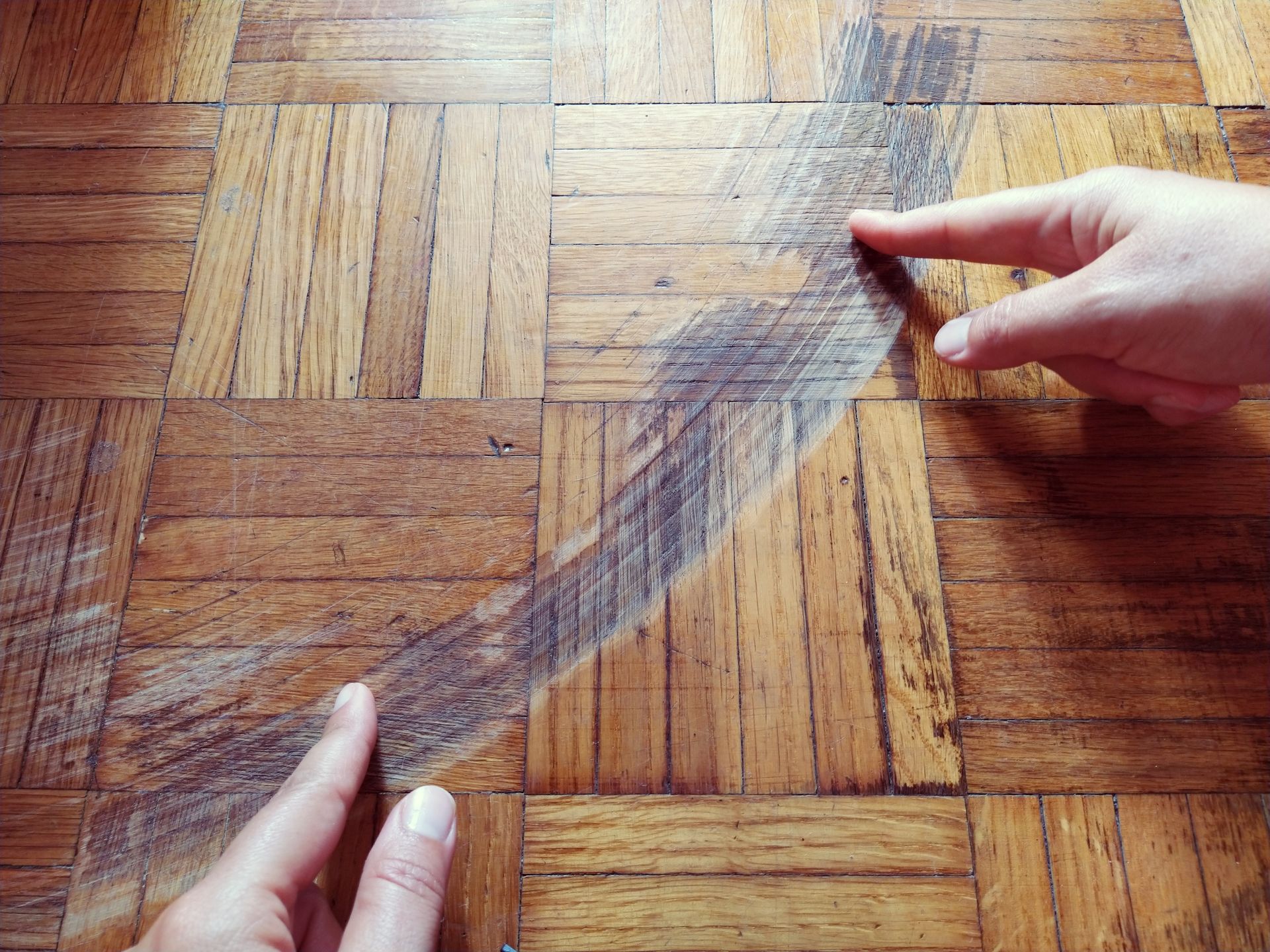 Une main montrant des traces de frottement sur un parquet en bois.