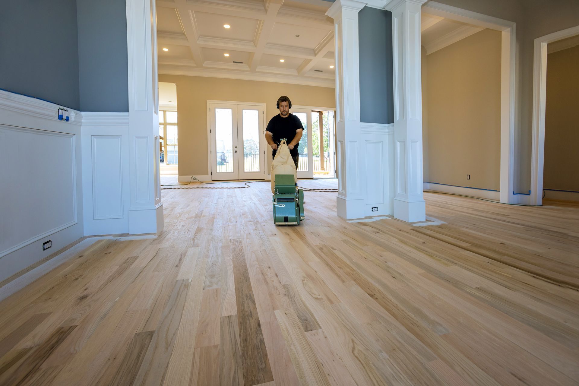 Une personne ponce un parquet clair dans une pièce vide récemment rénovée.