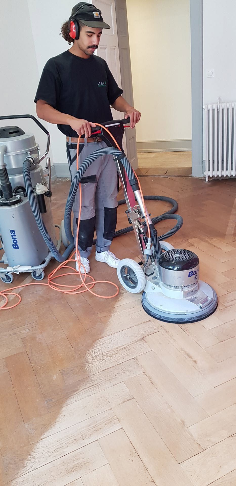 Un ouvrier utilisant une ponceuse à parquet dans une pièce équipée d’un aspirateur et dotée d’un plancher en bois.
