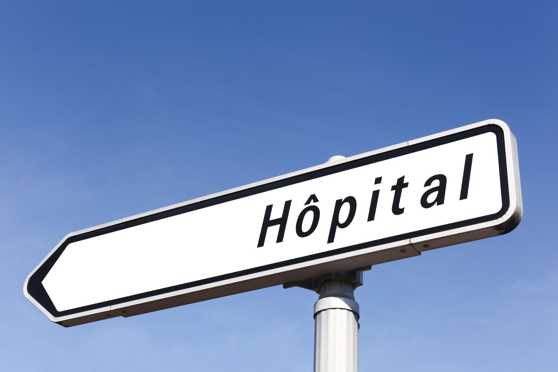 Panneau indicateur pointant à gauche vers Hôpital, sous un ciel bleu.