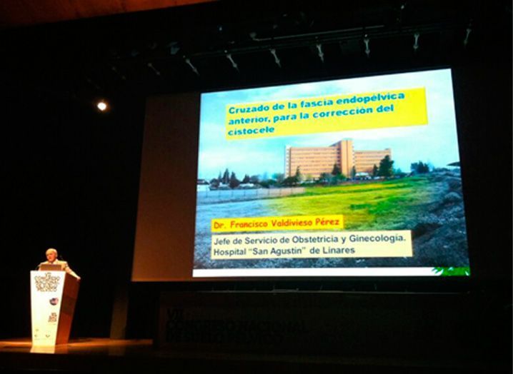 Un hombre está de pie en un podio frente a una pantalla grande.