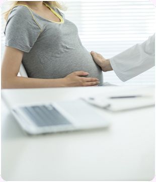 Una mujer embarazada está sentada en un escritorio hablando con un médico.