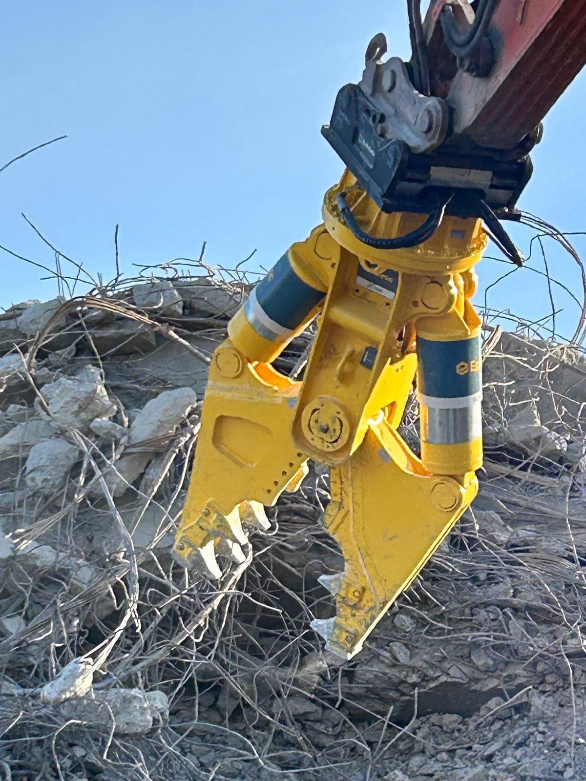 Ein gelber Bagger schneidet sich durch einen Betonhaufen.