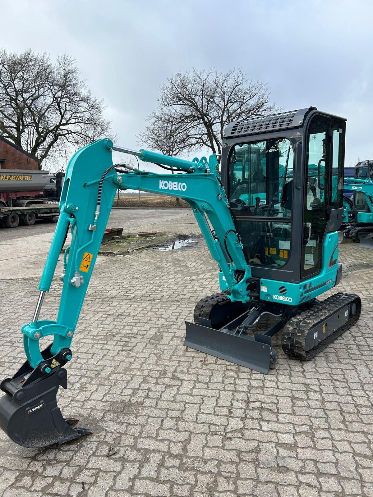 Ein kleiner blauer Bagger steht auf einem Ziegelsteinpflaster.