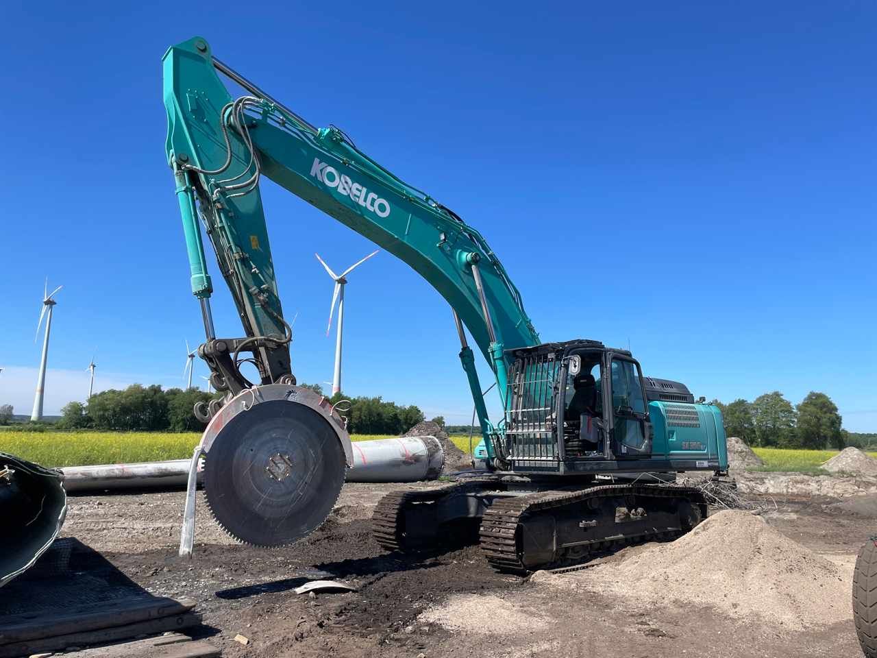 Ein großer Bagger schneidet ein Rohr in den Boden.