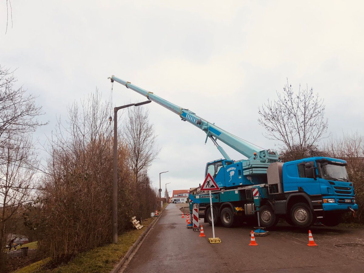 Ein blauer Lastwagen mit einem daran befestigten Kran steht am Straßenrand.