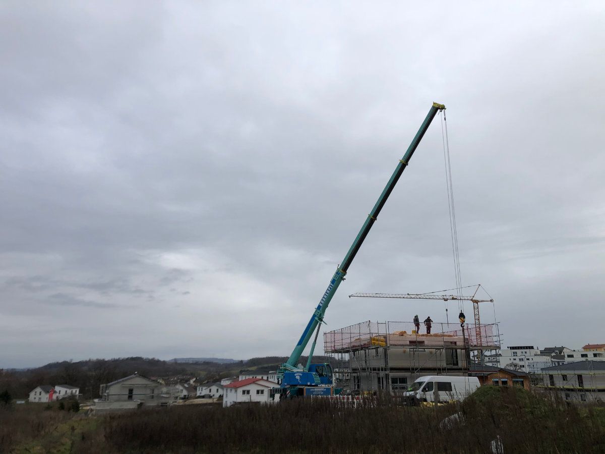 An einem bewölkten Tag hebt ein Kran das Dach eines Gebäudes an