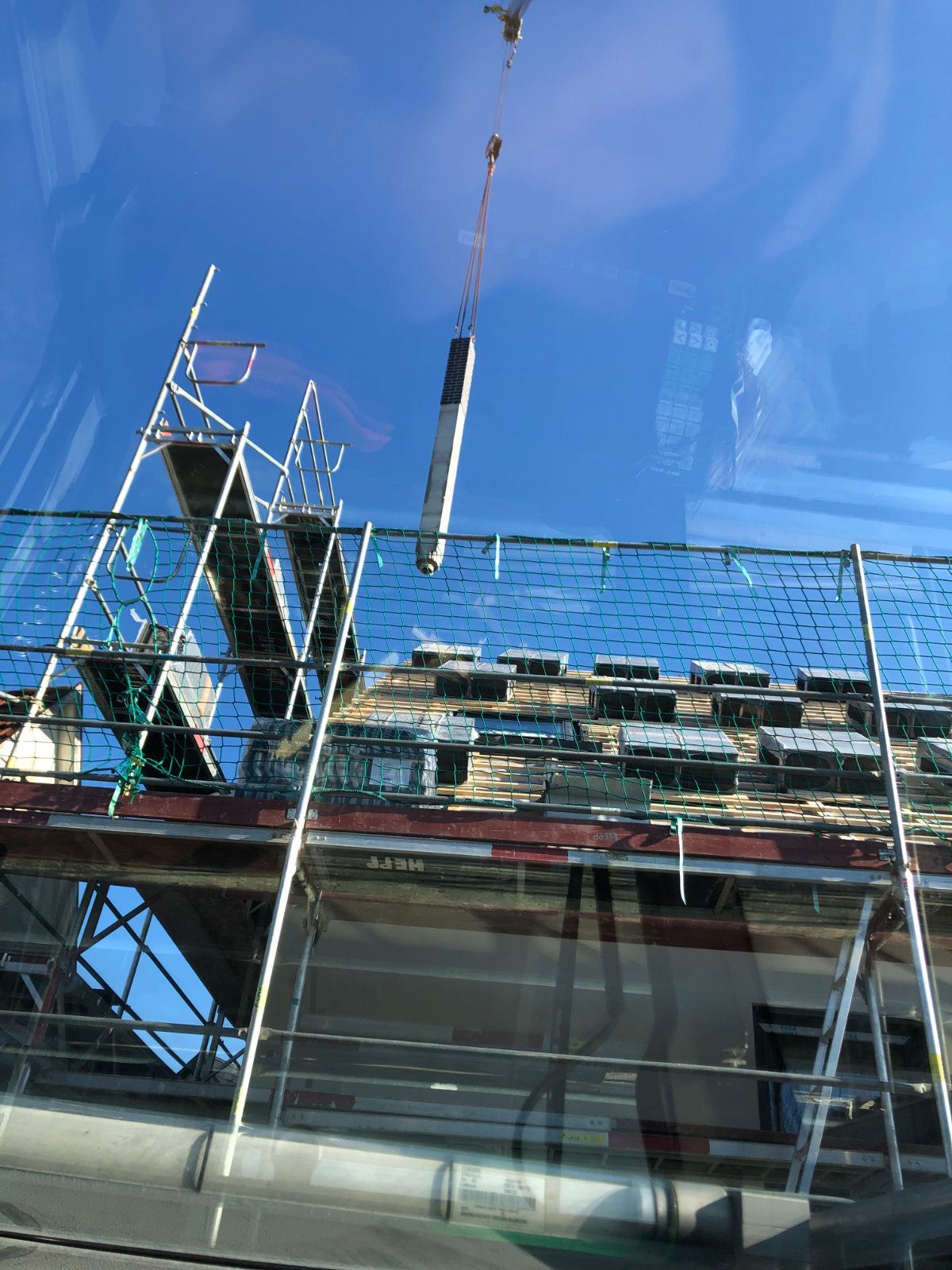 Ein Kran hebt ein Stück Holz vom Dach eines Gebäudes.