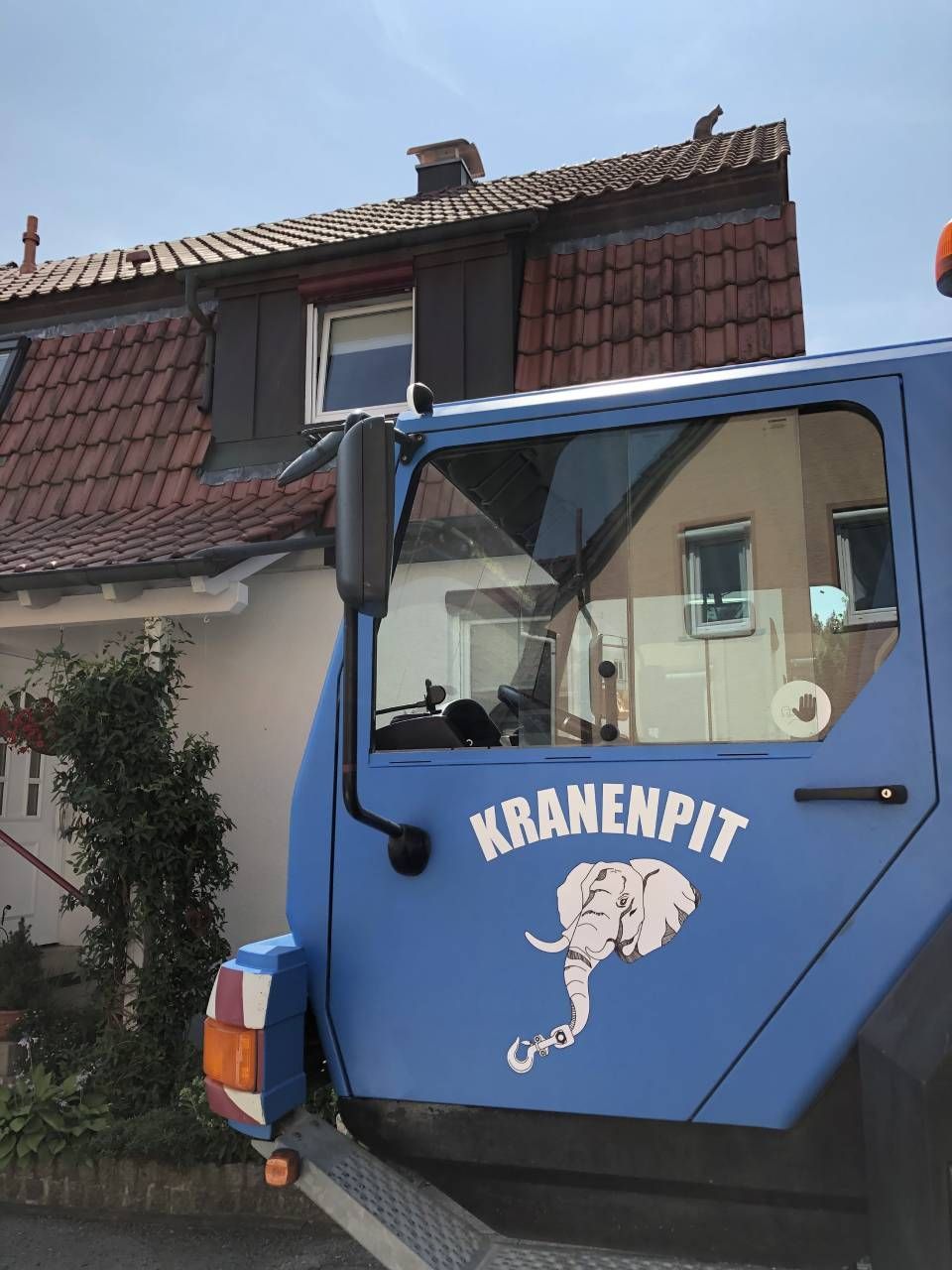 Ein blauer Kranenpit-LKW steht vor einem Haus
