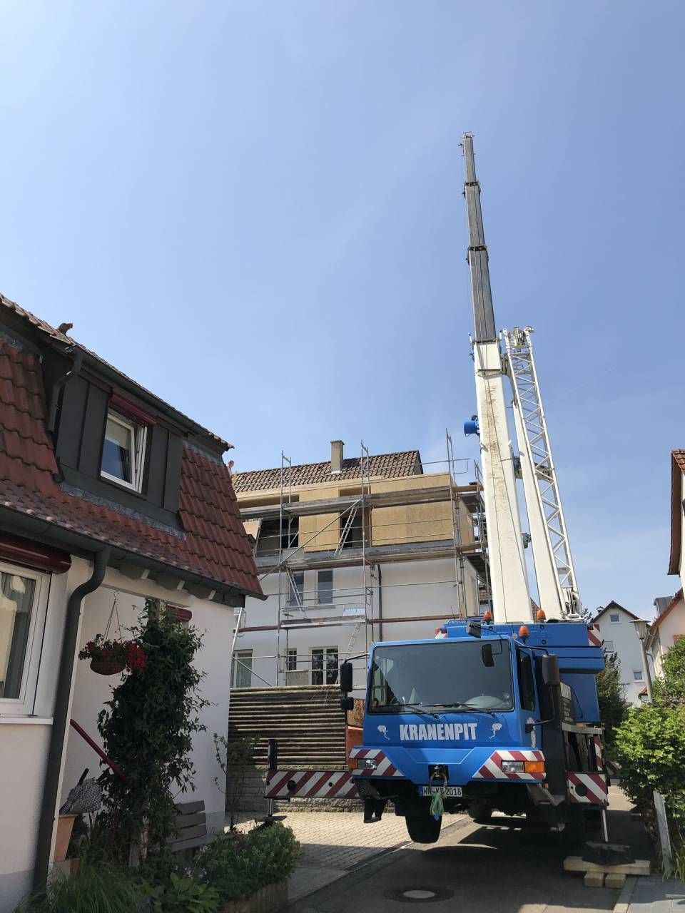 Ein blauer Lastwagen mit einem Kran darauf steht vor einem Haus.