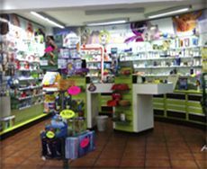 Vista interior de una farmacia con estantes llenos de productos para la salud, un mostrador central de cajas y azulejos marrones.
