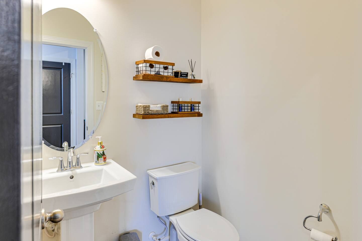 A bathroom with a sink , toilet , mirror and shelves.