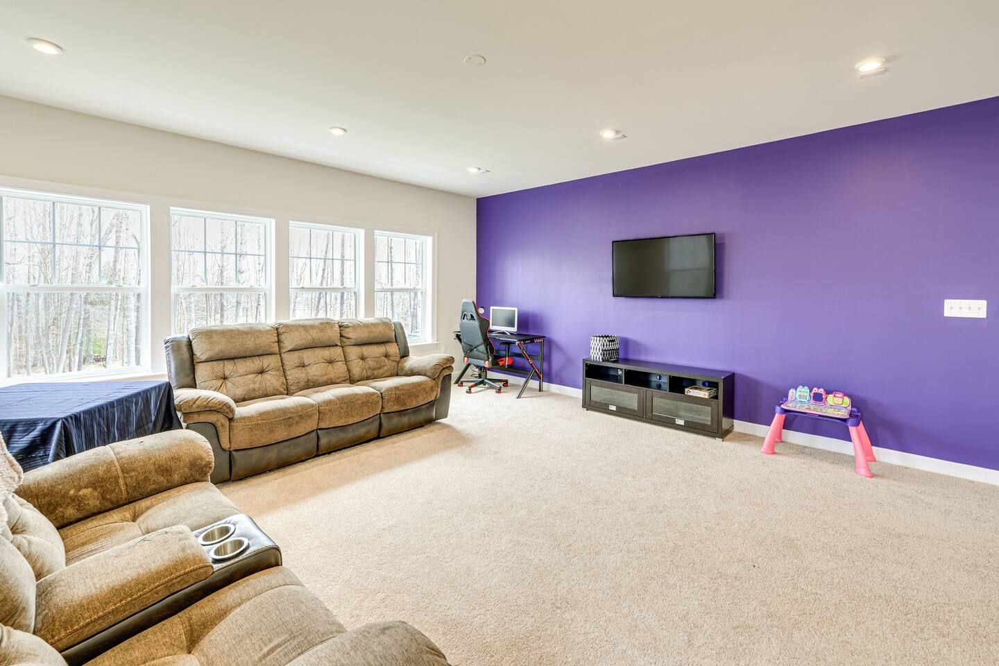A living room with purple walls , a couch , chairs and a flat screen tv.